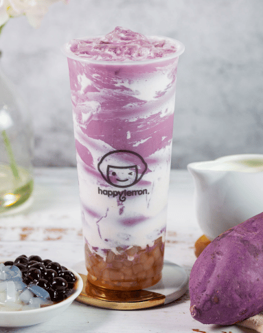 A tall clear cup with purple and white swirled bubble tea, tapioca pearls at the bottom, and the "happylemon" logo. A purple sweet potato, a jug of milk, and two bowls of toppings are nearby.
