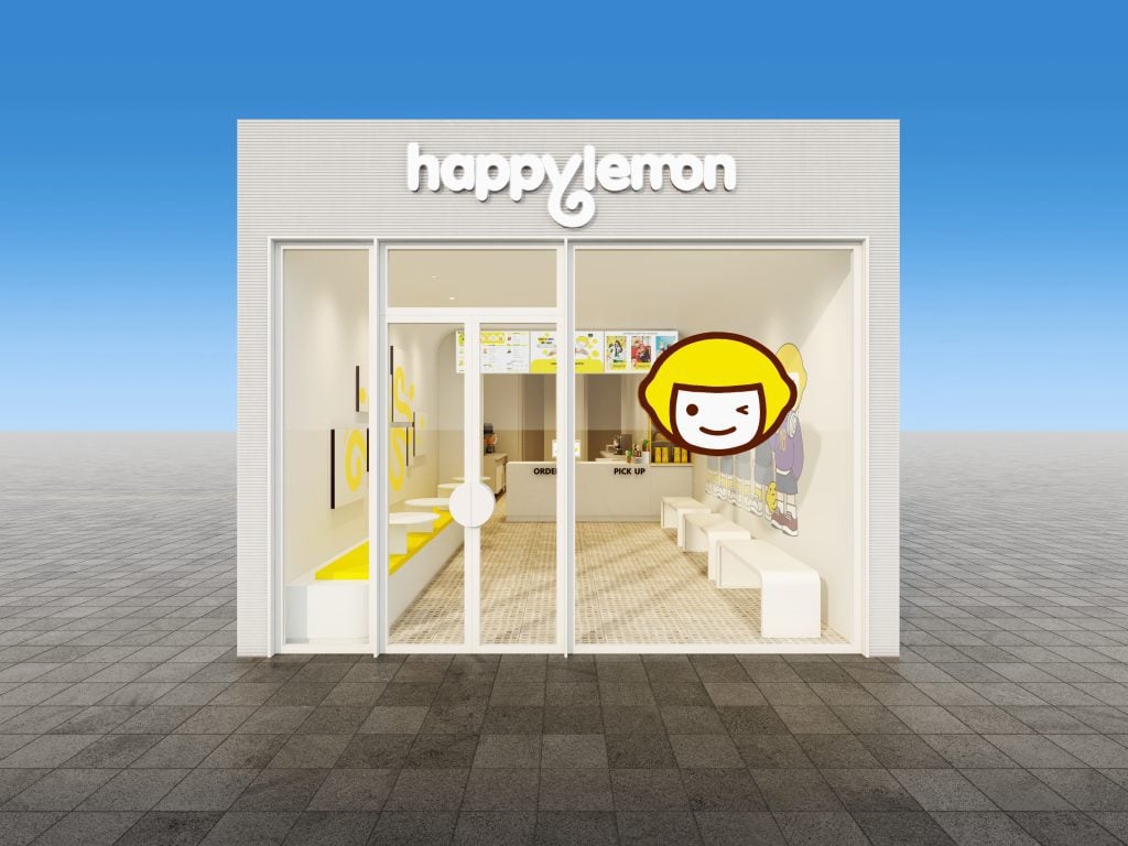 A storefront for "happylemon" with large glass windows, a white exterior, and a yellow cartoon face logo on the door. The interior has white furniture and menus above the counter. The sky is clear and blue.