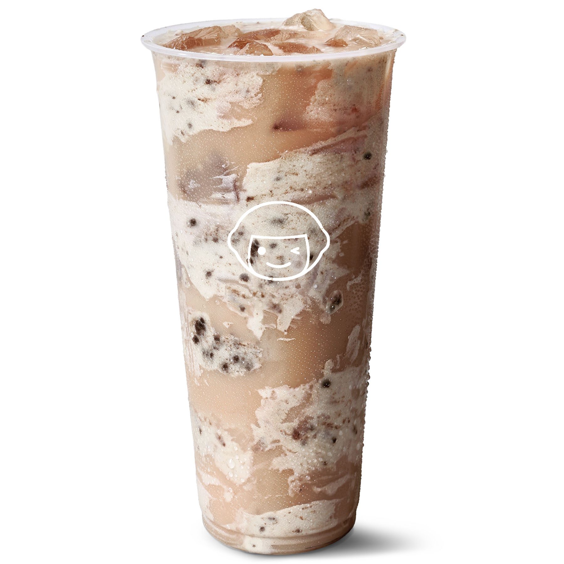 A large clear plastic cup filled with a swirled iced beverage that appears to contain milk, cookies, and cream, with ice cubes visible at the top. The cup has a simple line art logo printed on the front.