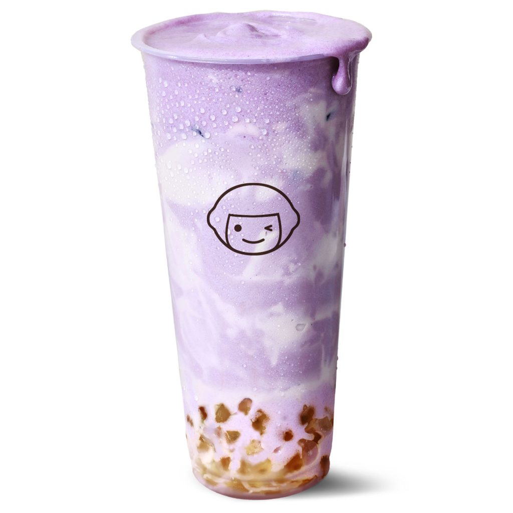A tall clear cup filled with a swirled purple and white drink, topped with foam, and tapioca pearls at the bottom. The cup has condensation and a cartoon face logo on the front.