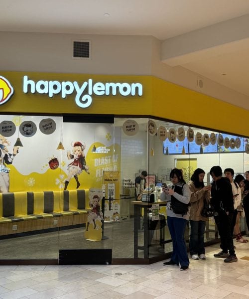 A group of people lines up in front of a Happylemon store in a mall. The storefront features bright yellow branding and anime-style character decorations on the windows and walls.